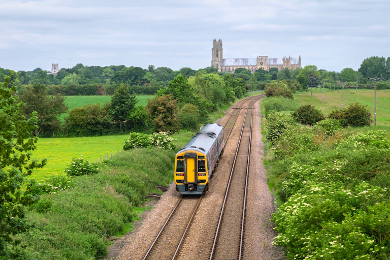 Train on tracks flanked by fields with church in background.