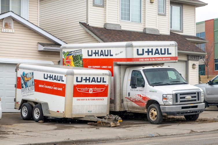 An orange and white U-Haul truck and storage pod in a driveway.
