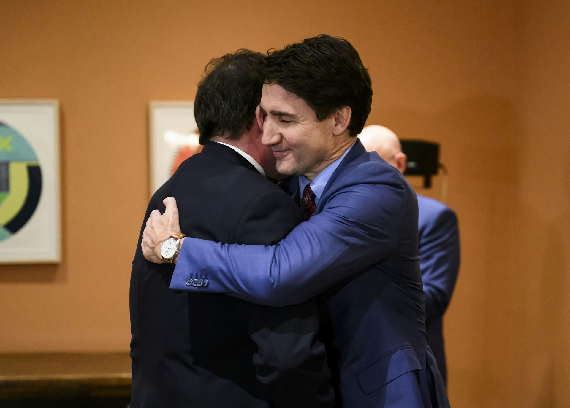 Two dark-haired men in suits embrace.