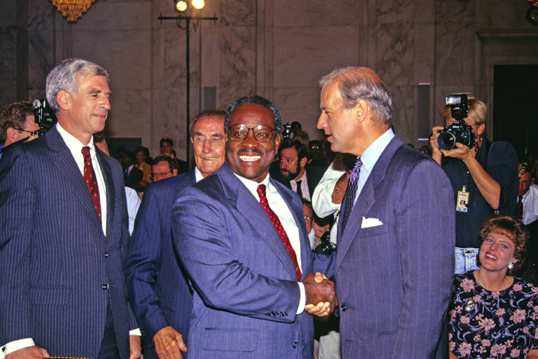 Two men in blue suits shaking hands in a large, crowded meeting room.