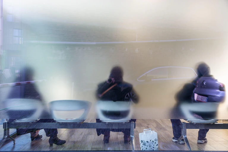 People on chairs seen through a fuzzy pane of glass.