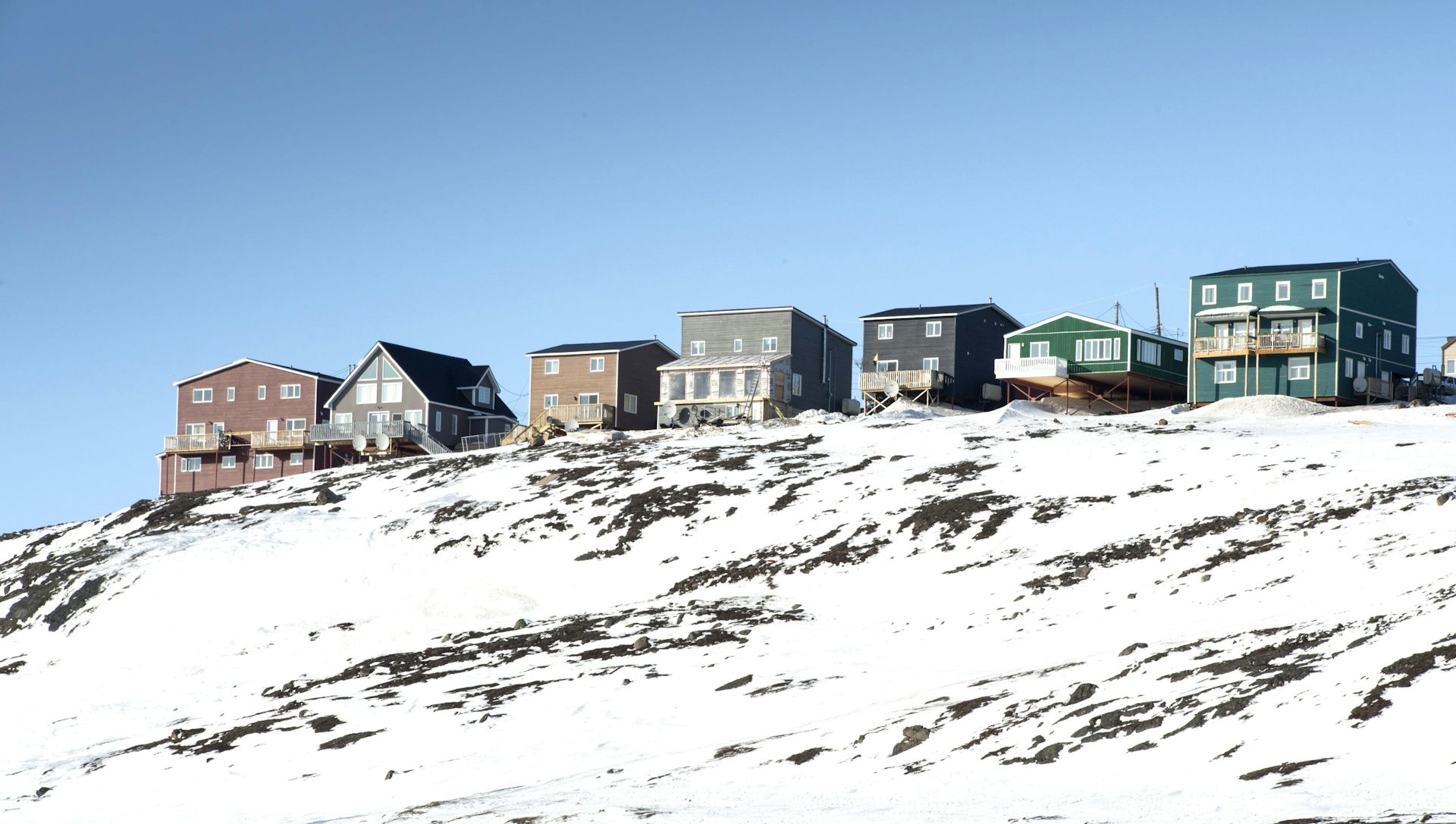 A row of houses on a snowy ridge under sunny skies.
