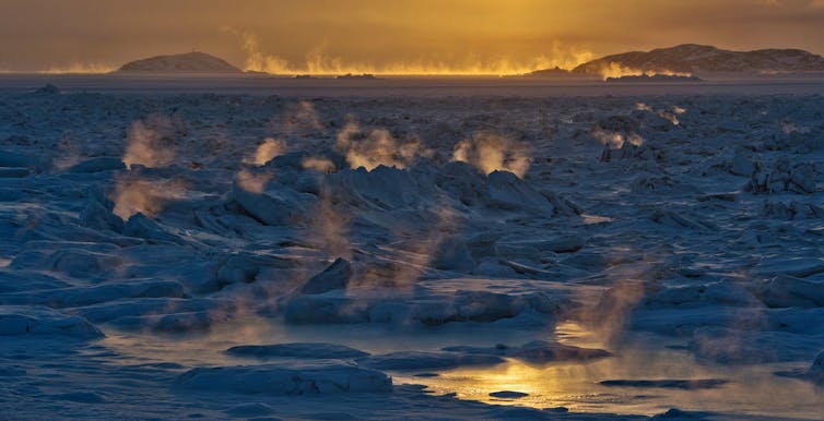 The sun sets over a steamy frozen bay.