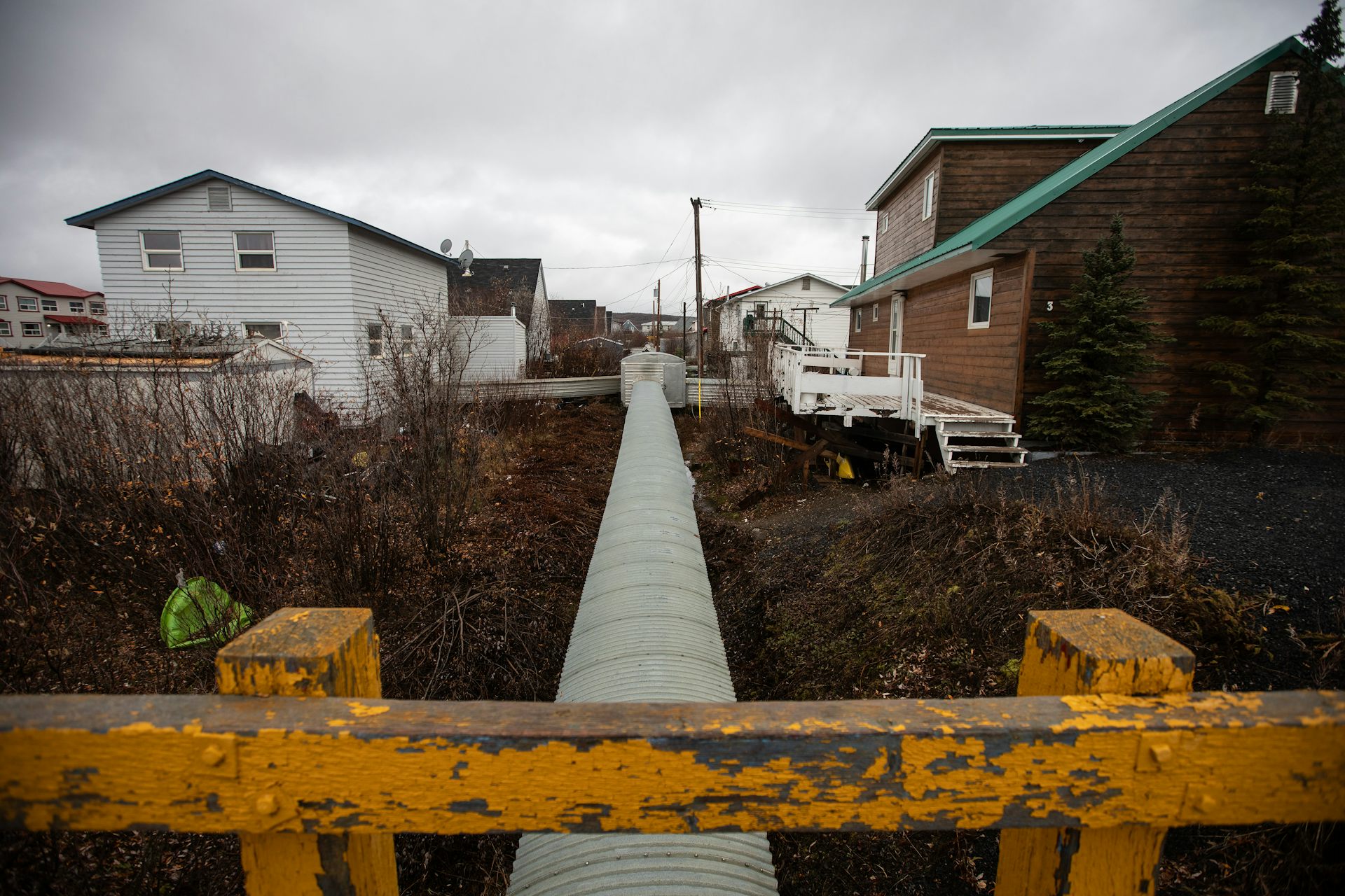 Above-ground water, sewer and utility lines with houses on either side.