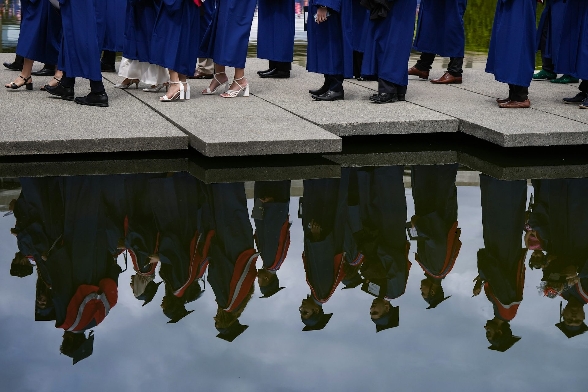A reflection of graduates on the move in a ceremonial line in water.