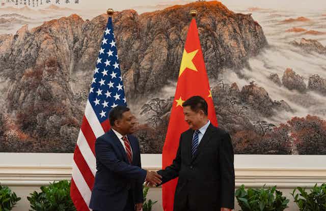 Two men shake hands in front of flags of China and the US