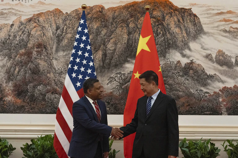 Two men shake hands in front of flags of China and the US