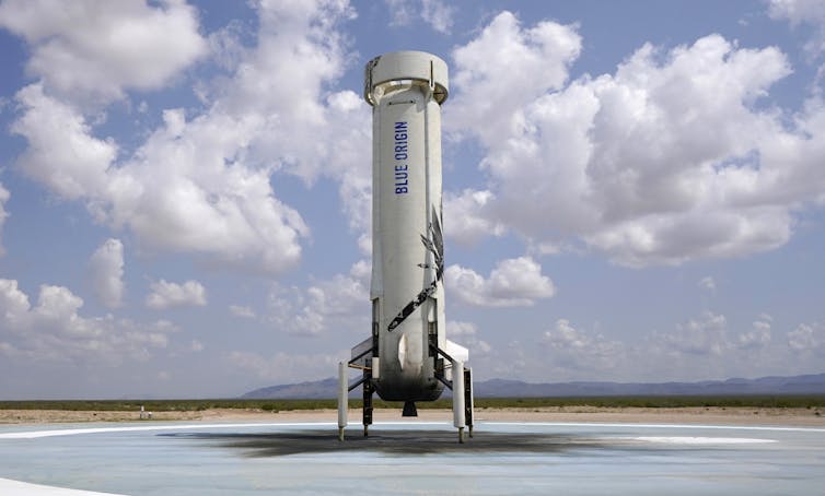 The New Shepard rocket, which looks like a cylinder with legs and a circular top, sitting on a landing pad.
