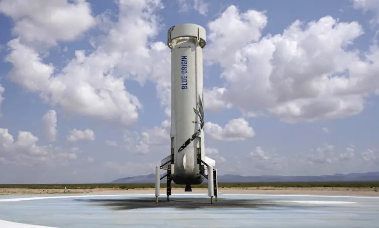 The New Shepard rocket, which looks like a cylinder with legs and a circular top, sitting on a landing pad.