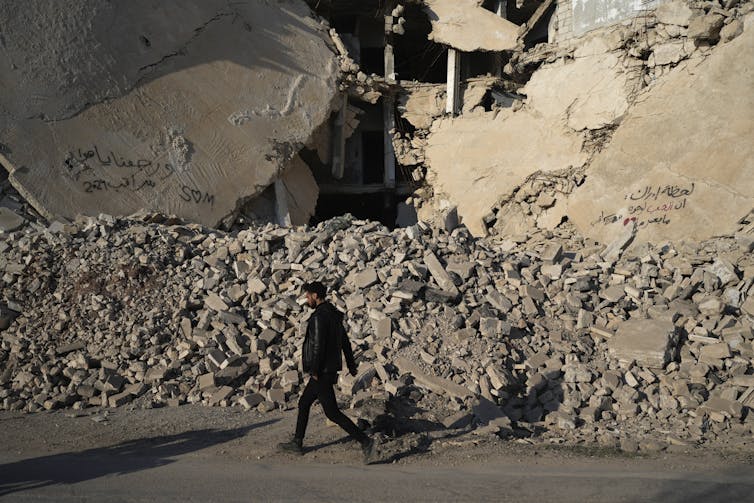 A man walks past the rubble of a destroyed building.