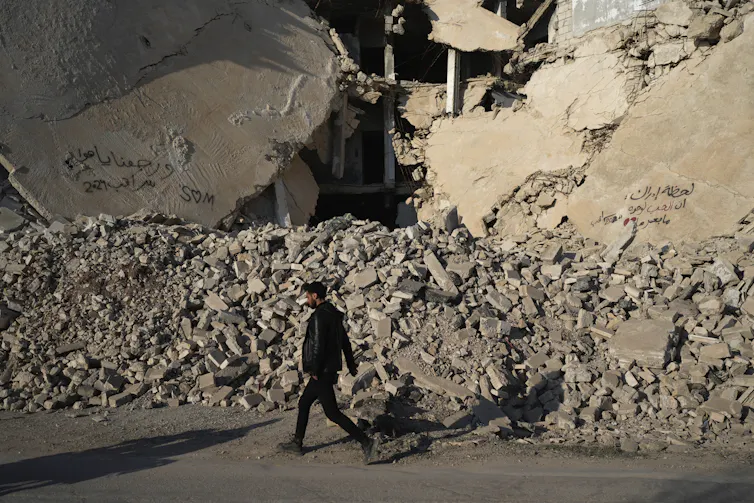 A man walks past the rubble of a destroyed building.