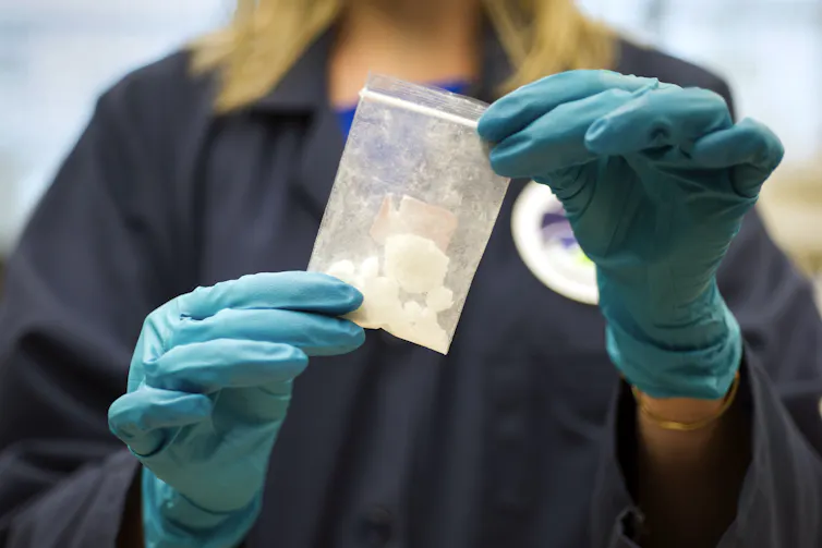 A person wearing gloves holds up a small plastic bag with a white rock-like subtance