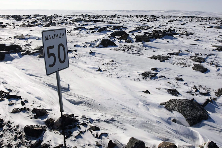 A speed limit sign is seen in a snowy, craggy expanse with no road visible.