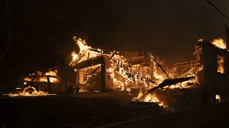 The remnants of a house and a car are seen engulfed in flames.