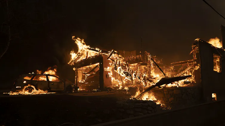 The remnants of a house and a car are seen engulfed in flames.