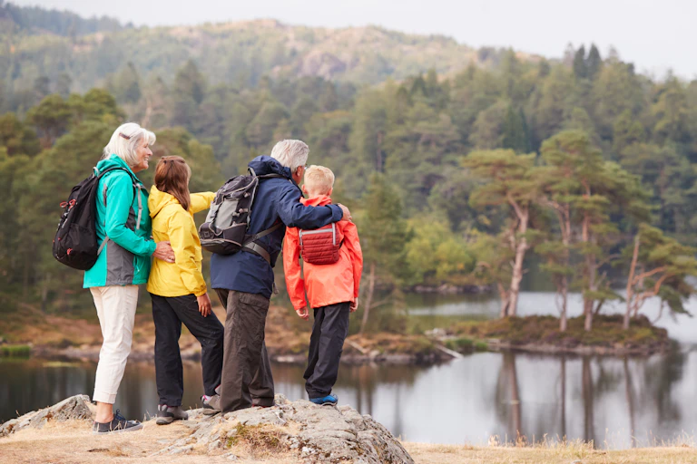 Two older people with two children standing by the edge of a lake