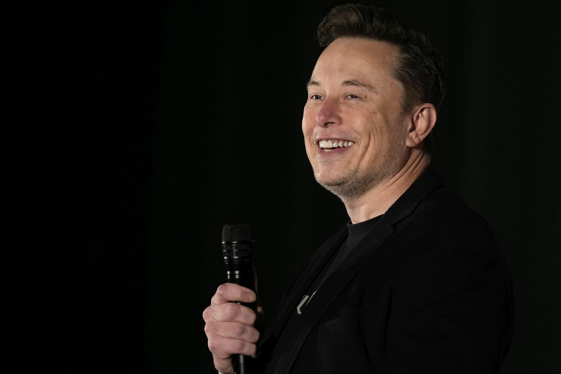 Elon Musk smiles while holding microphone