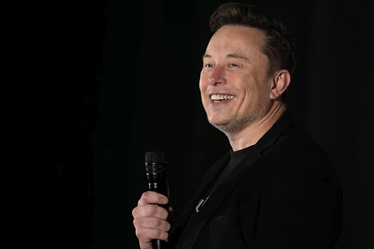 Elon Musk smiles while holding microphone