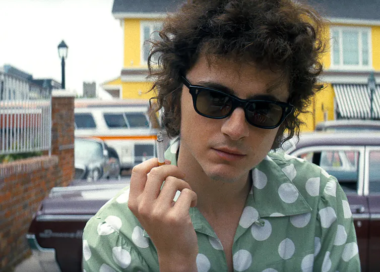Film still of a man with dark curly hair in a polka dot shirt.