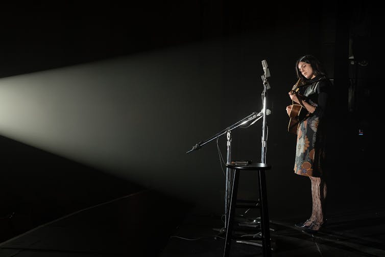 Film still: Joan plays a guitar on stage.