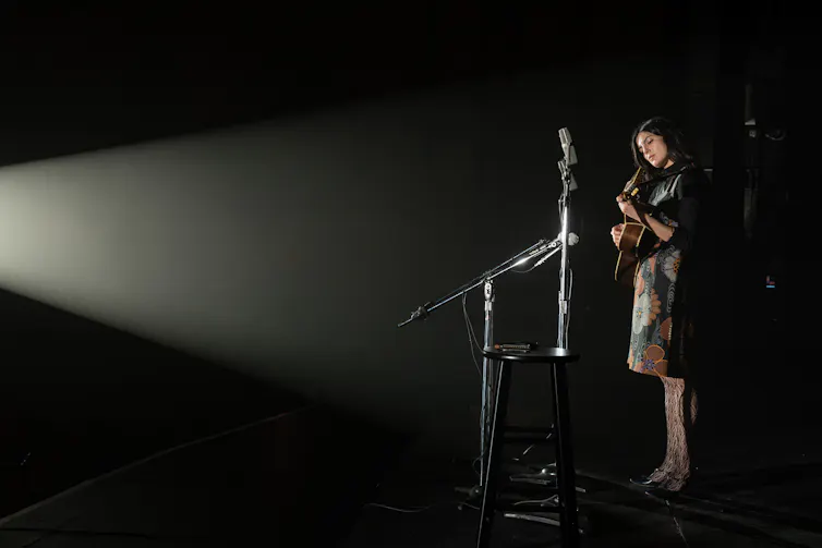 Film still: Joan plays a guitar on stage.