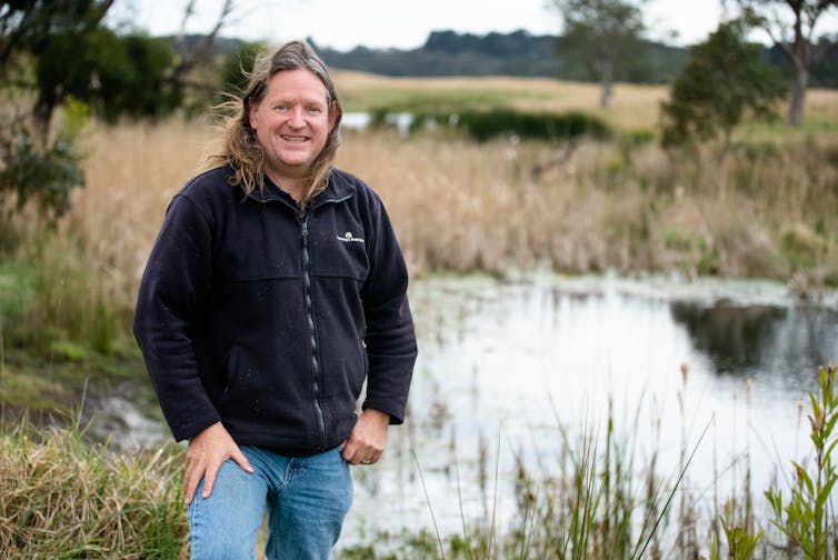 Man standing in front of a 'frog bog' wetland that looks like a farm dam in a natural setting