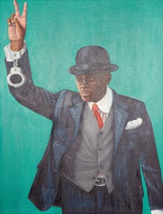 An African man in a suit and bowler hat holds up a hand, making a victory sign with his fingers. From his wrist hangs a pair of handcuffs.