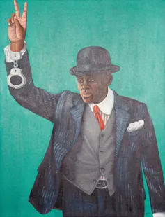 An African man in a suit and bowler hat holds up a hand, making a victory sign with his fingers. From his wrist hangs a pair of handcuffs.