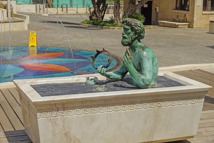 A statue of Archimedes in a bath, holding a crown.