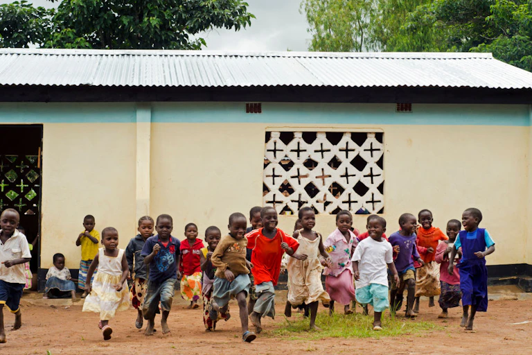Young children run towards the camera from a building