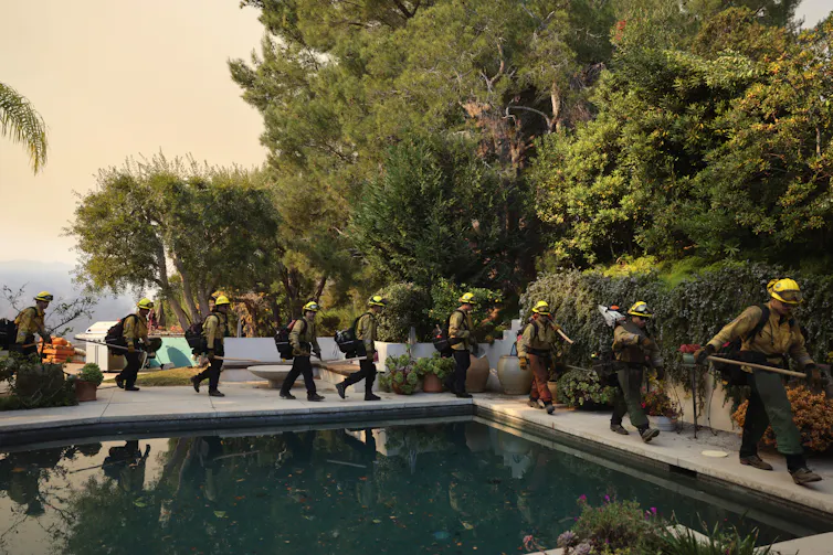 A procession of firefighters marches past a backyard pool.