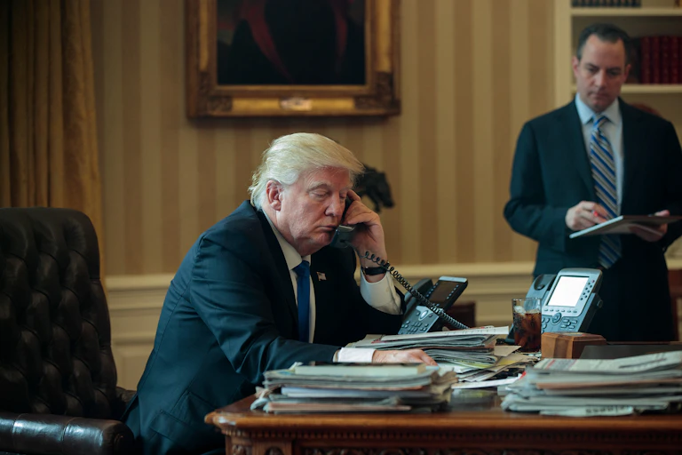 Donald Trump assis dans le Bureau oval et tenant le combiné d’un téléphone.