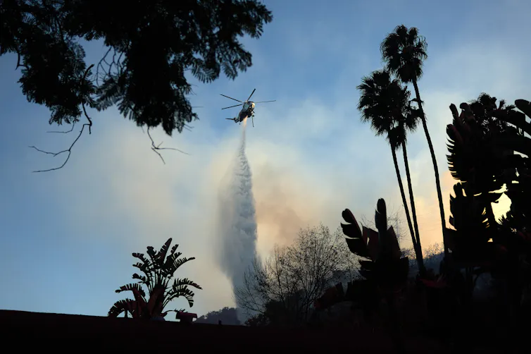 An aircraft dumps water on a smoky hillside.