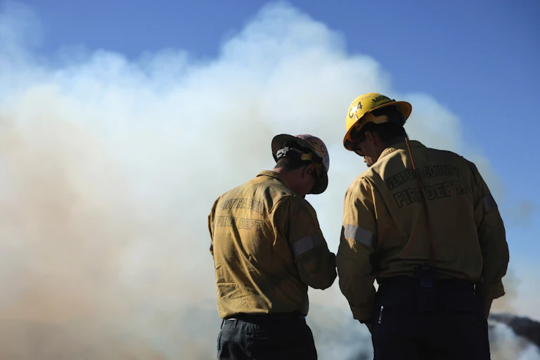 Two firemen stand before a smoky horizon.