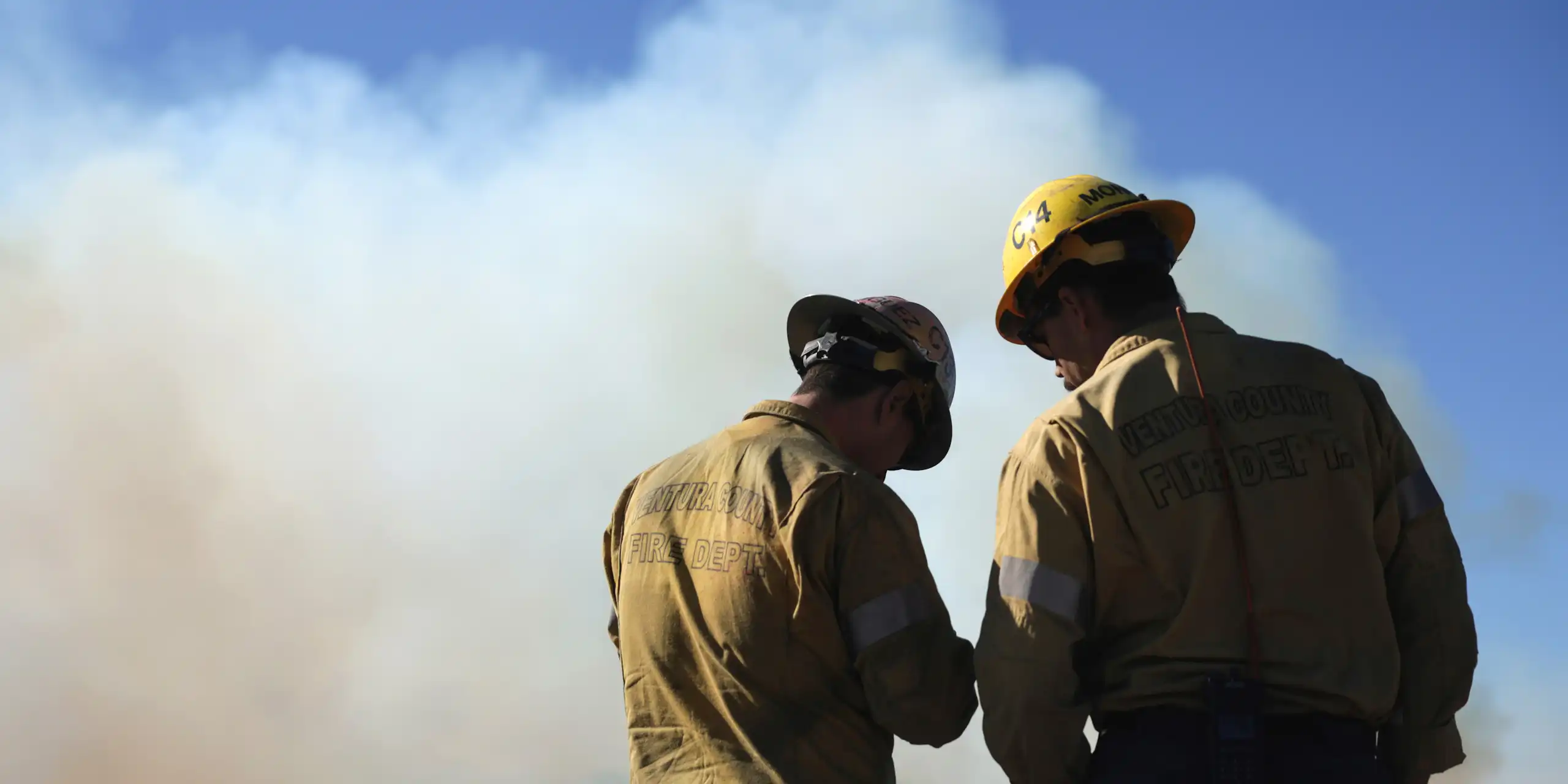 Two firemen stand before a smoky horizon.