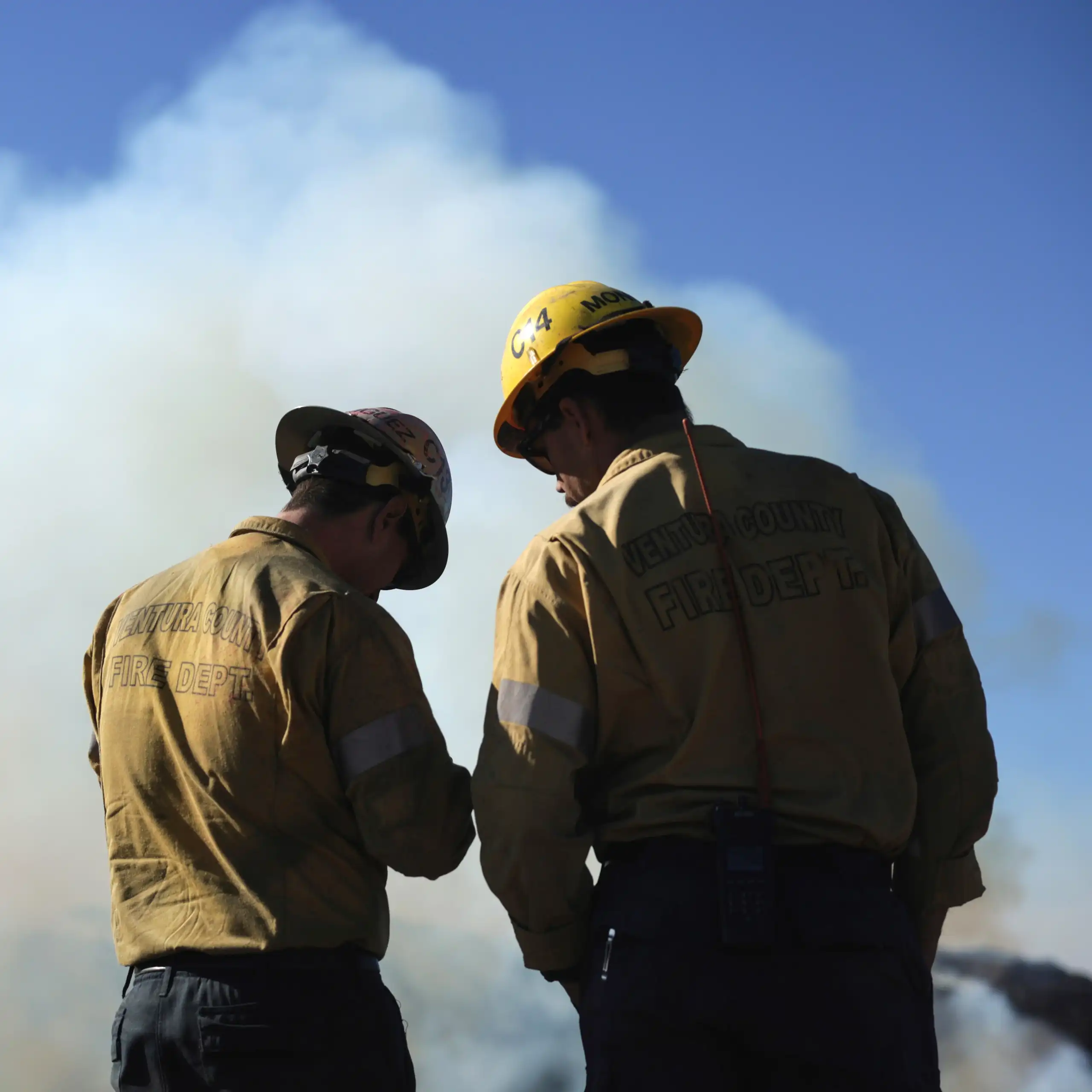 Two firemen stand before a smoky horizon.