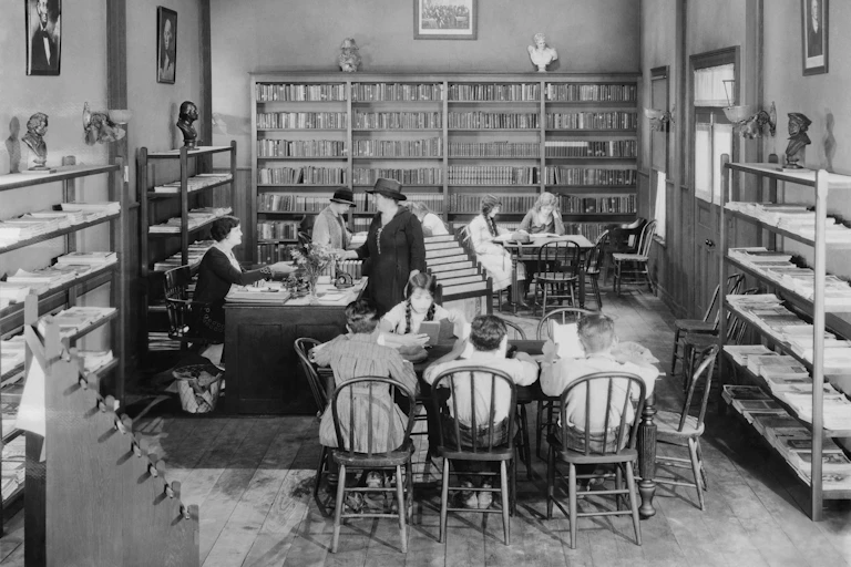 Un grupo de mujeres y niños estudian en la sala de una biblioteca.