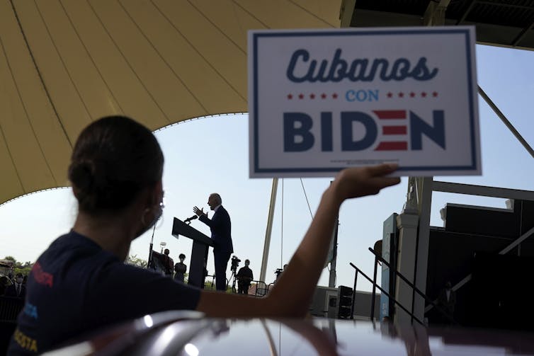 The silhouette of a man holding a sign reading 'Cubanos con Biden'.