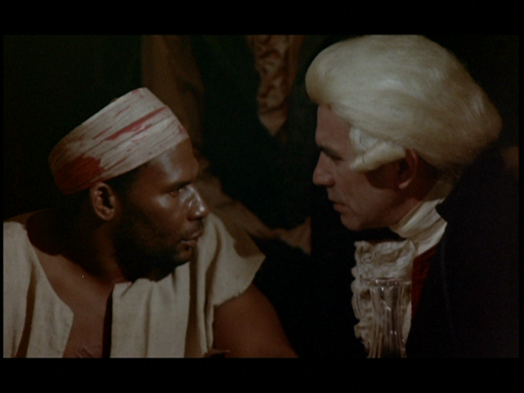 A Black man in white clothing speaking to a white man wearing a powdered wig