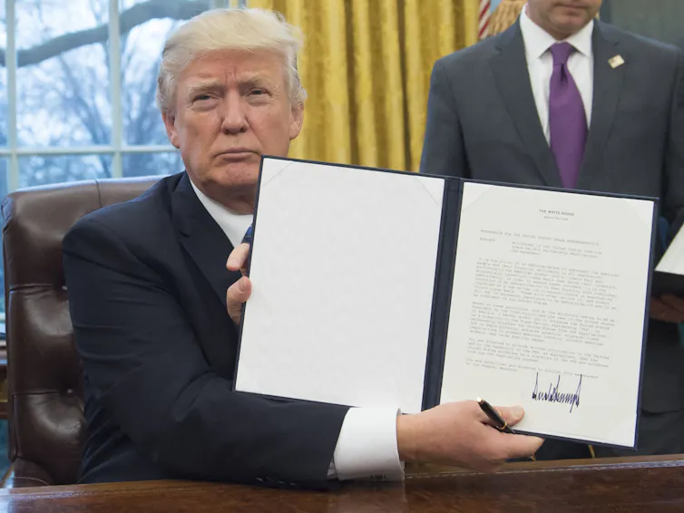 A man holds up a folder with pieces of paper showing a large signature in black ink.z