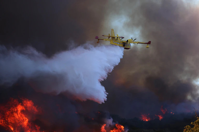 Um avião despeja água em uma encosta em chamas