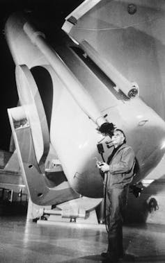 A black and white photo of a man looking through the lens of a large telescope.