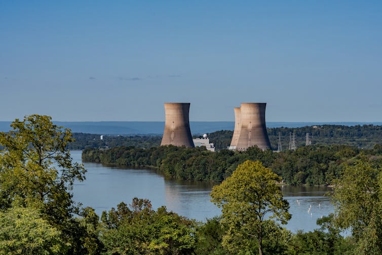 Two nuclear reactors seen in the distance behind a tree-lined river