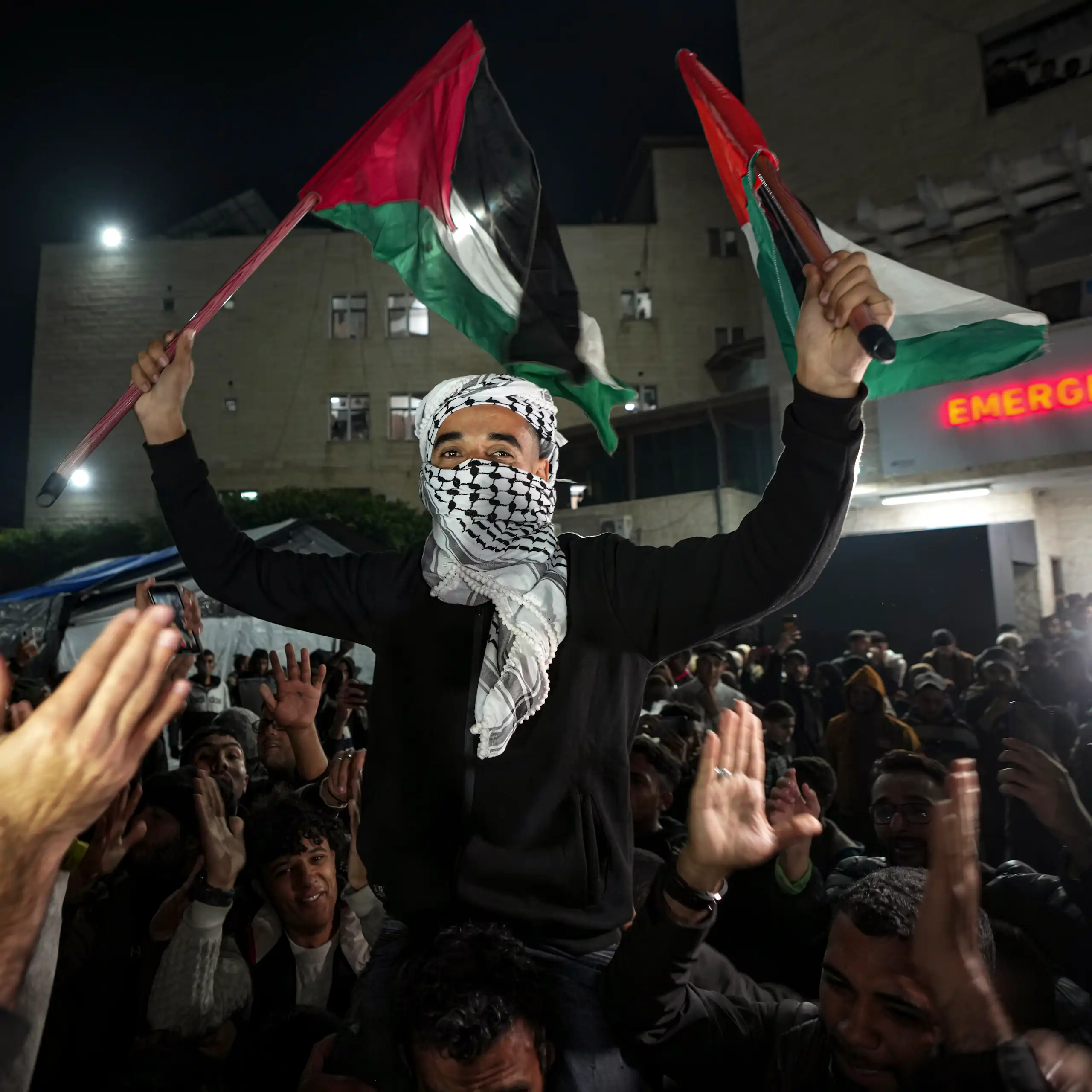 A Palestinian man celebrating and waving flags in a crowd