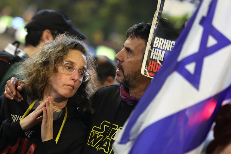 A man and women wave a blue and white Israeli flag.