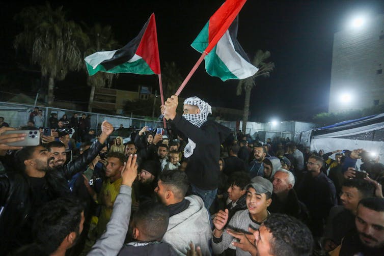A man in a headscarf holds aloft a red, green and white flag.
