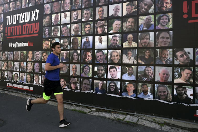 A man in shorts runs past a wall with people's faces on it.