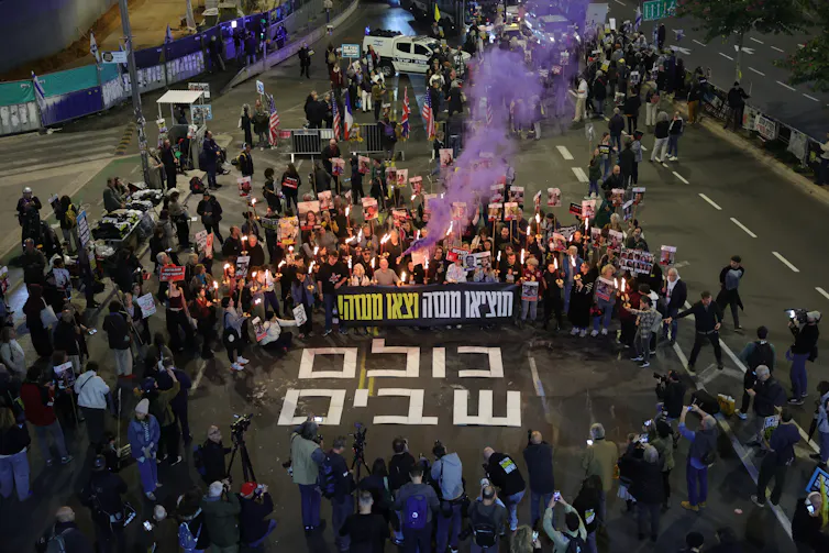 Uma grande multidão de pessoas se reuniu em uma rua israelense com cartazes.