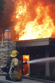 A firefighter directs a water hose at flames engulfing a chimney