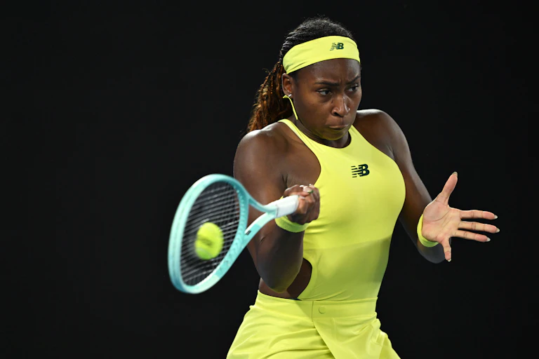African American woman in bright yellow sports attire hitting a forehand during a tennis match.